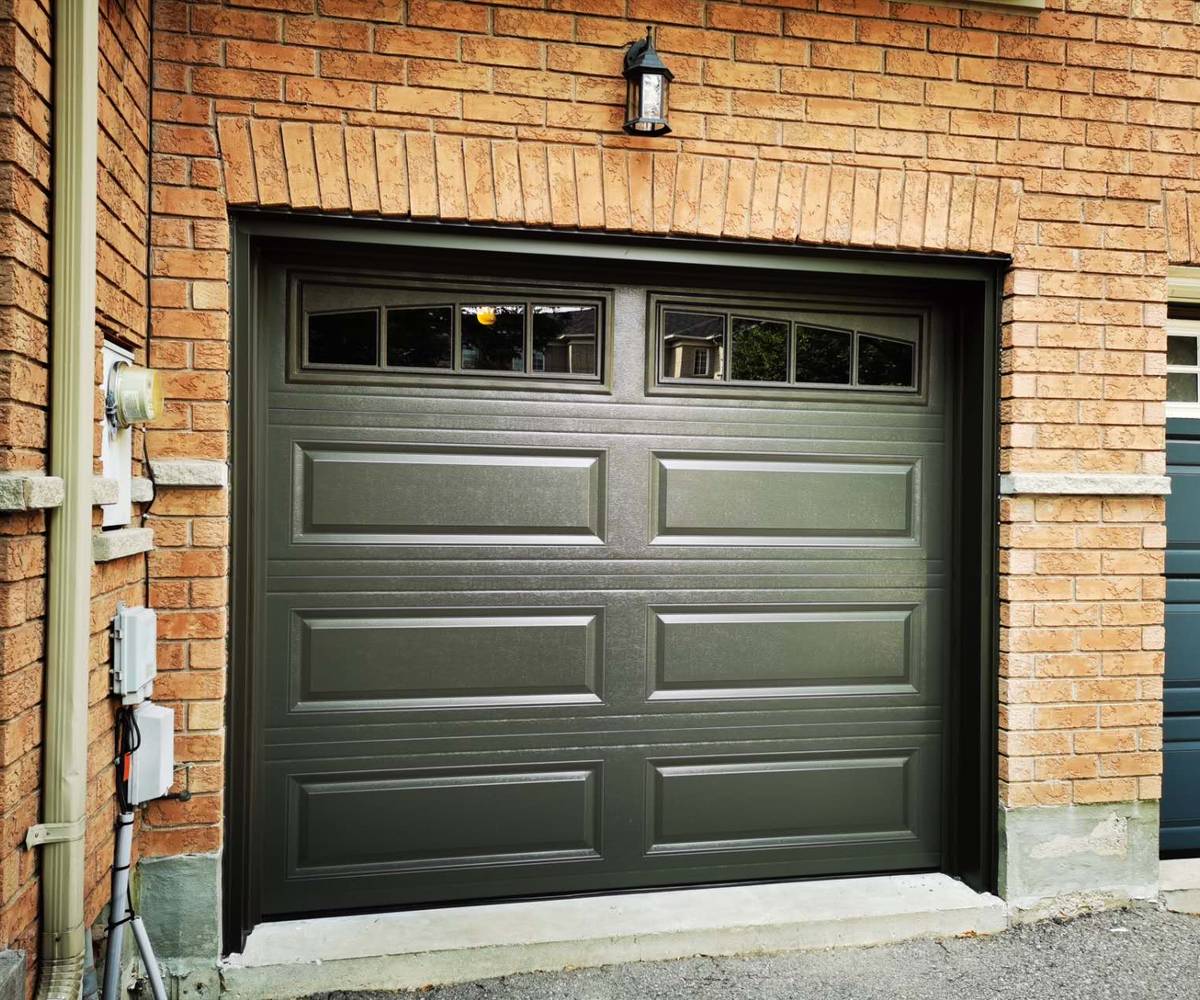 New dark green raised-panel garage door with arched window inserts after replacement